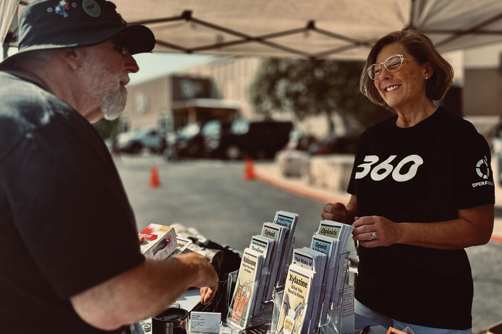 Operation 360 volunteer educating veteran attendee about opioid awareness resources at a community outreach event in Texas.